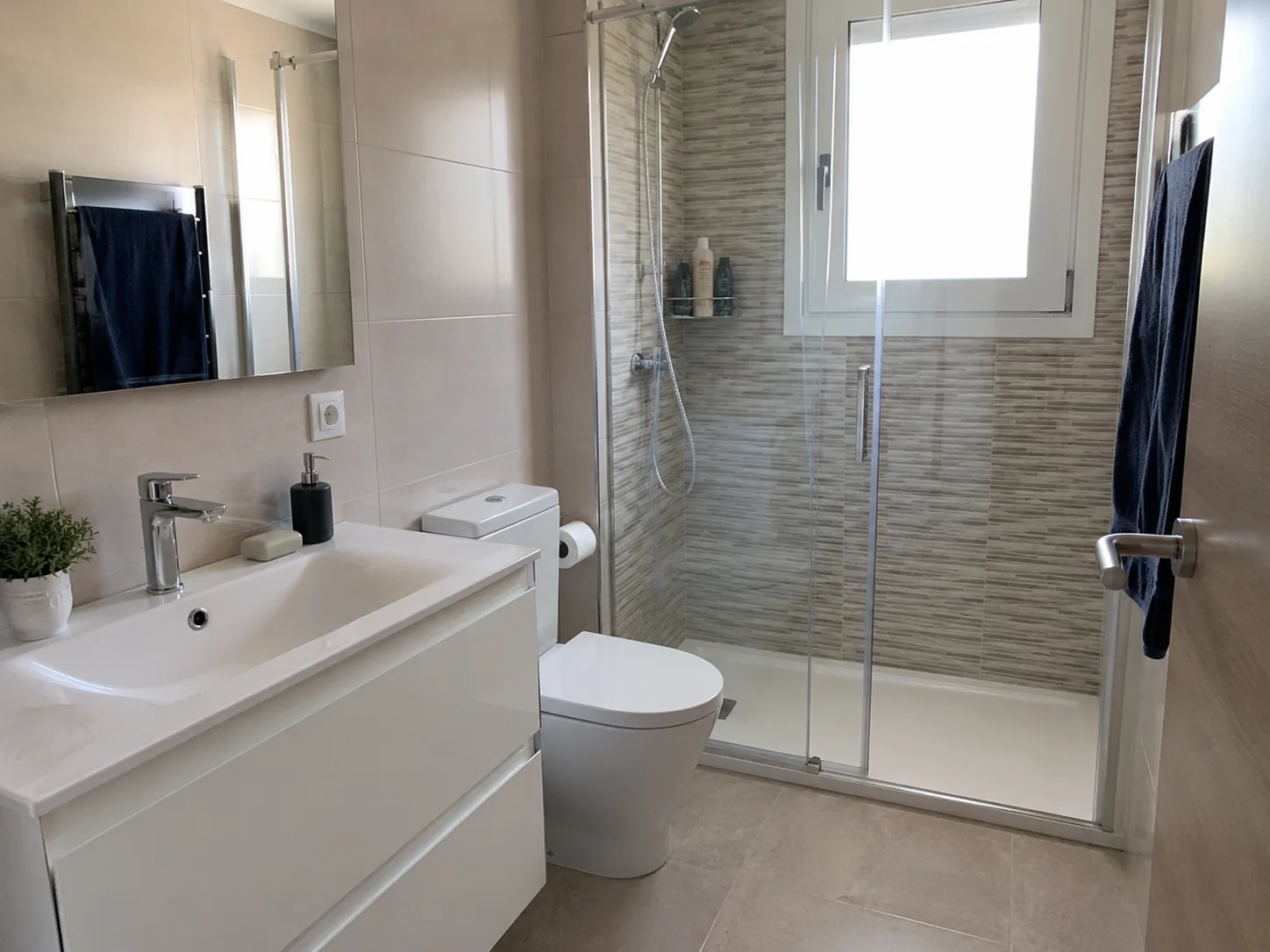 Baño limpio con mampara, lavabo, ducha y sanitarios cuidados